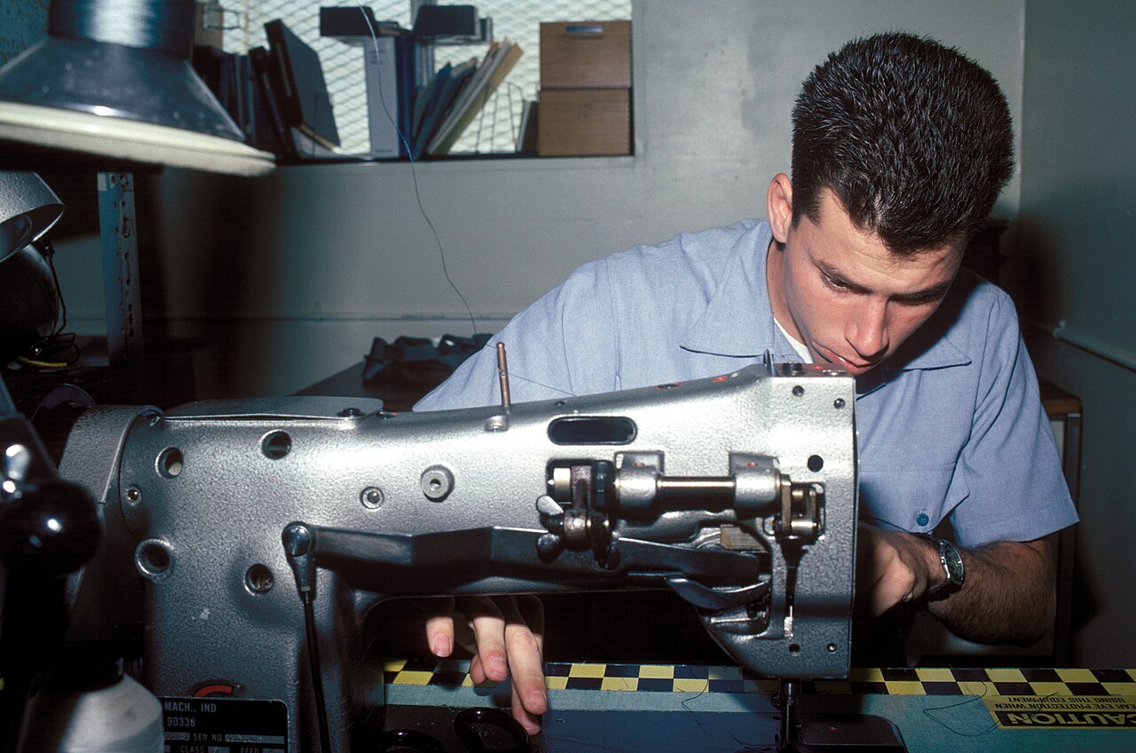 Técnico militar enhebrando una máquina de coser industrial para tejido pesado